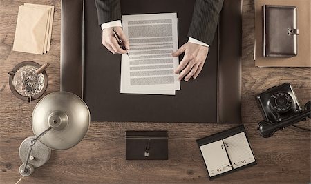 Vintage businessman in the office reading and signing a contract sitting at his desk, top view Stock Photo - Budget Royalty-Free & Subscription, Code: 400-08749459