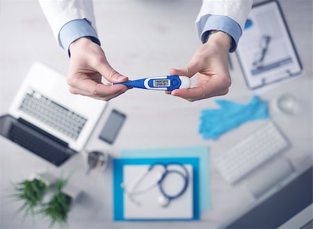 simsearch:400-08751444,k - Doctor measuring temperature and holding a digital thermometer, desktop with medical equipment and computer on background, top view Photographie de stock - Aubaine LD & Abonnement, Code: 400-08749507