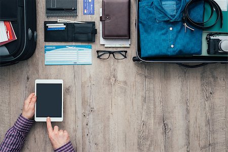 simsearch:400-09222181,k - Man packing for a trip, he is using a digital touch screen tablet and booking flights online using a mobile app, flat lay banner Fotografie stock - Microstock e Abbonamento, Codice: 400-08751434