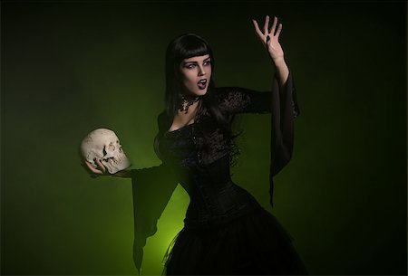 simsearch:400-07776243,k - Sensual witch in a corset and black velvet costume holding a skull in her hand, studio shot Fotografie stock - Microstock e Abbonamento, Codice: 400-08775195