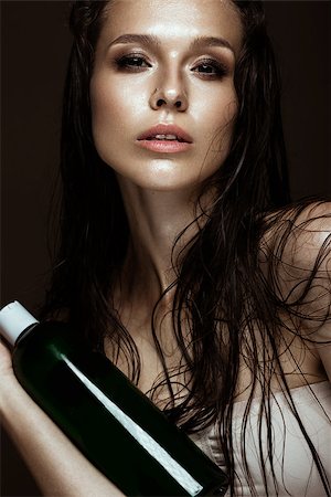 Beautiful girl with a bright make-up and wet hair and skin with bottle of cosmetic products in the hands. Beauty face. Picture taken in the studio on a black background. Photographie de stock - Aubaine LD & Abonnement, Code: 400-08771087