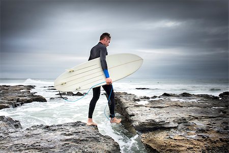 A man crosses the rocks and cravises on his way to the surf while holding a surf board in his arm. Photographie de stock - Aubaine LD & Abonnement, Code: 400-08795096