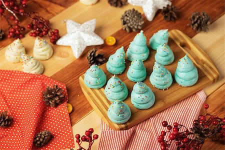 shyrix (artist) - Colored meringue in the form of Christmas trees, placed on a wooden butcher. On the table are pine cones, mountain ash, and various Christmas decorations. Stockbilder - Microstock & Abonnement, Bildnummer: 400-08795625