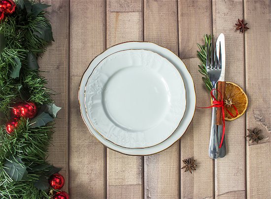 Christmas table layout, red tape with a cinnamon stick, rosmarin and a slice of dry orange on the light wooden background with christmas decorations Stock Photo - Royalty-Free, Artist: komarina, Image code: 400-08795859