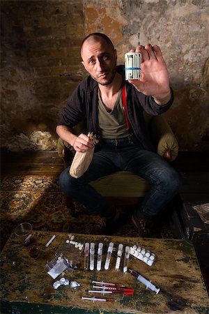 Drug dealer showing profit from selling drugs and injections. Many heavy drugs represented on table in front of him. Photographie de stock - Aubaine LD & Abonnement, Code: 400-08796661