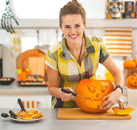 simsearch:400-07172678,k - Frightful Treats on the way. Portrait of smiling modern housewife in the Halloween decorated kitchen carving a big orange pumpkin Jack-O-Lantern Photographie de stock - Aubaine LD & Abonnement, Code: 400-08792497
