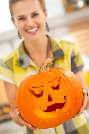 simsearch:400-07172678,k - Frightful Treats on the way. Smiling modern housewife in the Halloween decorated kitchen showing big pumpkin Jack-O-Lantern. Closeup Photographie de stock - Aubaine LD & Abonnement, Code: 400-08792508