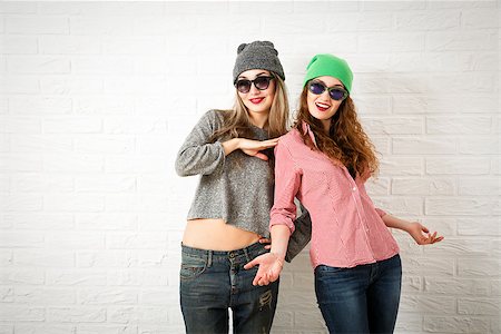 simsearch:400-08430017,k - Two Happy Smiling Hipster Girls Posing at White Brick Wall Background. Trendy Casual Fashion Woman Outfit in Autumn or Spring. Teenage Female Friendship and Lifestyle. Toned Photo with Copy Space. Stock Photo - Budget Royalty-Free & Subscription, Code: 400-08814066