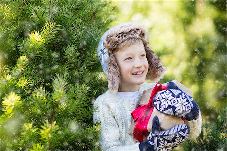 snow cosy - beautiful smiling boy in trapper hat, sweater and mittens holding nicely wrapped christmas gift by the tree or in the forest enjoying snowy cold winter weather, holiday or happiness concept Stock Photo - Budget Royalty-Free & Subscription, Code: 400-08815276