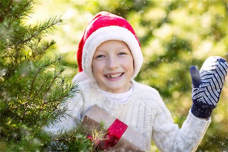 snow cosy - beautiful smiling boy in santa's hat, sweater and mittens holding nicely wrapped christmas gift by the tree or in the forest enjoying snowy cold winter weather, holiday or happiness concept Stock Photo - Budget Royalty-Free & Subscription, Code: 400-08815280