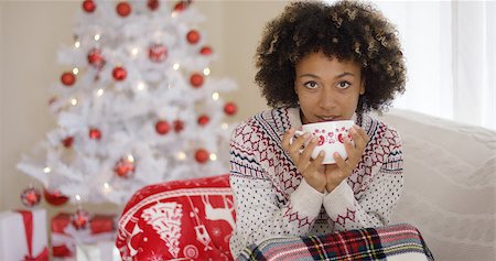 Pretty woman in sweater sipping from cup while seated on sofa. White Christmas tree with red ornaments and gifts in background. Stock Photo - Budget Royalty-Free & Subscription, Code: 400-08810049
