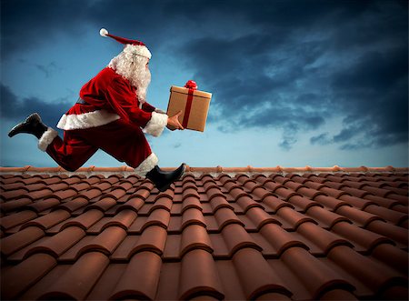 Santa Claus runs with a big present on a house roof Stock Photo - Budget Royalty-Free & Subscription, Code: 400-08810157