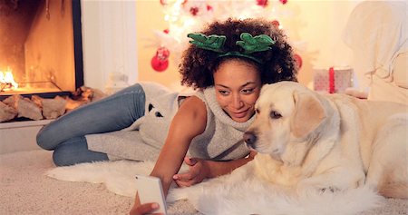 people adult fireplace fun - Cute young woman wearing a colorful green set of Christmas reindeer antlers taking a selfie with her dog as they relax in the living room in front of the fire. Stock Photo - Budget Royalty-Free & Subscription, Code: 400-08811131