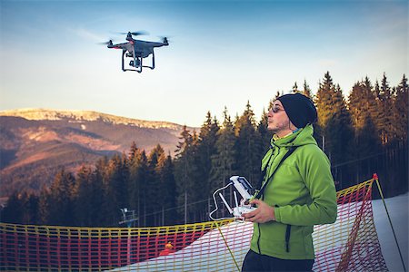 Young man in green jacket operating a drone using a remote controller. Ski resort in the background, winter landscape with pine tree forest and mountains. Bukovel, Carpathians, Ukraine, Europe. Exploring beauty world Stock Photo - Budget Royalty-Free & Subscription, Code: 400-08863237