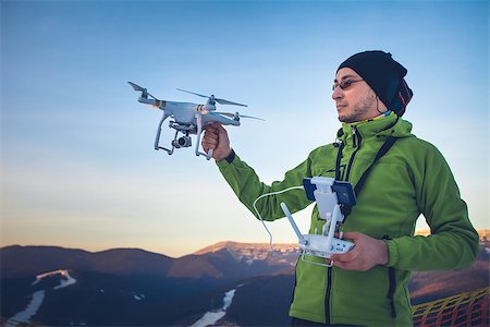 Young man in green jacket holding a drone and remote controller. Ski resort in the background, winter landscape with pine tree forest and mountains. Bukovel, Carpathians, Ukraine, Europe. Exploring beauty world Stock Photo - Budget Royalty-Free & Subscription, Code: 400-08863238
