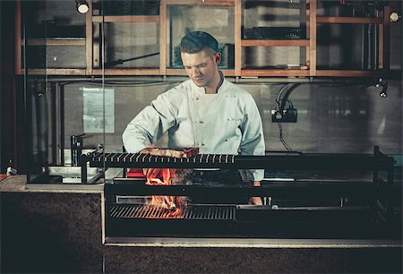 Young white chef in apron standing near the brazier whith coals. Man cooking beef steak in the interior of modern professional kitchen Stock Photo - Budget Royalty-Free & Subscription, Code: 400-08863239