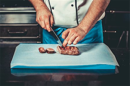 simsearch:400-07713408,k - Chef in hotel or restaurant kitchen dressed in blue apron cooking, only hands, he is cutting meat or steak with big sharp knife Stock Photo - Budget Royalty-Free & Subscription, Code: 400-08863246