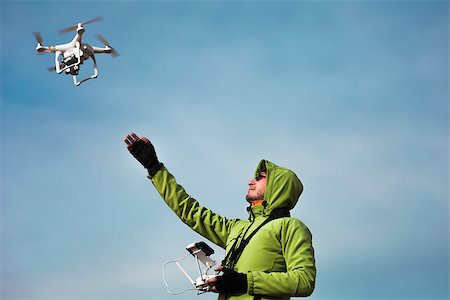 Young man in green jacket operating a drone using a remote controller. Blue sky in the background, winter holidays in mountains. Bukovel, Carpathians, Ukraine, Europe. Exploring beauty world Stock Photo - Budget Royalty-Free & Subscription, Code: 400-08863885