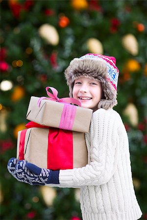 snow cosy - positive smiling child in trapper hat and warm winter clothes holding christmas gifts enjoying christmas time by the tree Stock Photo - Budget Royalty-Free & Subscription, Code: 400-08887765