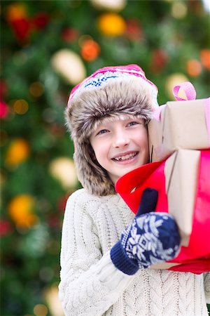 snow cosy - positive smiling child in trapper hat and warm winter clothes holding christmas gifts enjoying christmas time by the tree Stock Photo - Budget Royalty-Free & Subscription, Code: 400-08887766