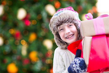 snow cosy - positive smiling child in trapper hat and warm winter clothes holding christmas gifts enjoying christmas time by the tree Stock Photo - Budget Royalty-Free & Subscription, Code: 400-08887762