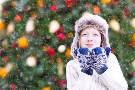 snow cosy - positive smiling child in trapper hat and warm winter clothes blowing snow, having fun and enjoying christmas time by the tree Stock Photo - Budget Royalty-Free & Subscription, Code: 400-08888148
