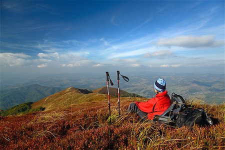 Tourist  looking at landscape. Halt in mountains. Woman has bright red outdoorsy clothing. Sky and mountain ranges in background. Red  bilberry leaves in foreground. Sticks and backpack near woman. Fotografie stock - Microstock e Abbonamento, Codice: 400-08889125