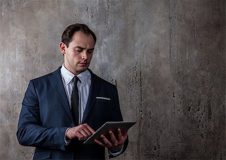 senior dark background - Portrait of a mature businessman with tablet in a suit on concrete gray wall background Stock Photo - Budget Royalty-Free & Subscription, Code: 400-08898941