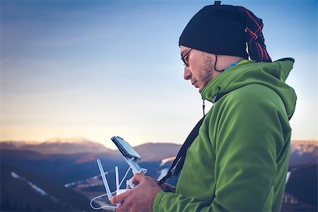 Young man in green jacket operating a drone using a remote controller. Ski resort in the background, winter landscape with pine tree forest and mountains. Bukovel, Carpathians, Ukraine, Europe. Exploring beauty world Stock Photo - Budget Royalty-Free & Subscription, Code: 400-08890825
