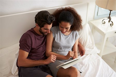 Couple Sitting On Bed Looking At Digital Tablet Together Stock Photo - Budget Royalty-Free & Subscription, Code: 400-08891791