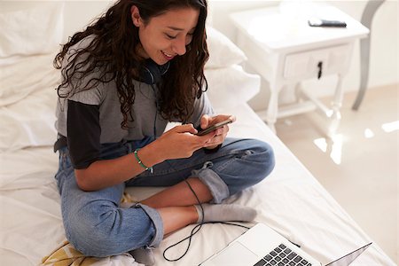simsearch:400-08892368,k - Teenage girl sitting on bed text messaging, elevated view Stock Photo - Budget Royalty-Free & Subscription, Code: 400-08892346