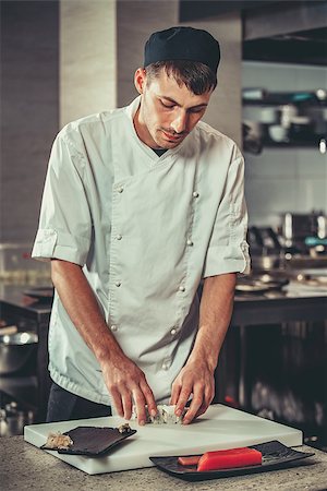 simsearch:400-08192842,k - Food: One young white chef dressed in white uniform decorate ready dish in restaurant. He is working on maki rolls. Preparing traditional japanese sushi set in interior of modern professional kitchen Foto de stock - Super Valor sin royalties y Suscripción, Código: 400-08893656