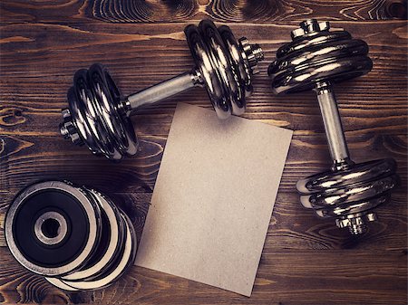 Toned image of metal dumbbells and a sheet of craft paper on a wooden background Stock Photo - Budget Royalty-Free & Subscription, Code: 400-08916437
