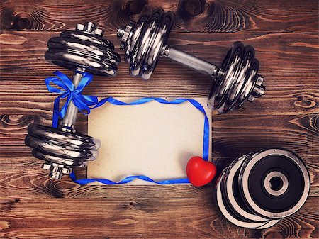 Toned image of metal dumbbells, blue atlas ribbon, red heart and a sheet of craft paper on a wooden background Stock Photo - Budget Royalty-Free & Subscription, Code: 400-08916438