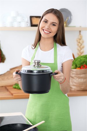 Young happy woman in a green apron cooking in the kitchen. Housewife found a new recipe for her soup. Healthy food and vegetarian concept. Stock Photo - Budget Royalty-Free & Subscription, Code: 400-08918132