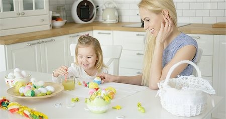 Smiling young woman helping little girl to color Easter eggs while sitting by table at light kitchen. Stock Photo - Budget Royalty-Free & Subscription, Code: 400-08962179