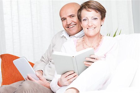 Loving happy middle-aged couple relaxing on a sofa reading at home, she with a book and the man with a tablet computer Stock Photo - Budget Royalty-Free & Subscription, Code: 400-09008793