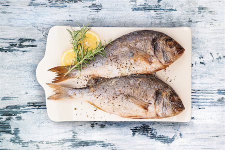 simsearch:400-07776969,k - Delicious grilled sea bream fish on kitchen board with rosemary, lemon and colorful peppercorns on white textured wooden background. Culinary healthy cooking. Stock photo. Foto de stock - Super Valor sin royalties y Suscripción, Código: 400-09008907