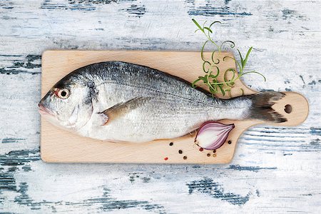 simsearch:400-07776969,k - Delicious fresh sea bream fish on wooden kitchen board with onion, rosemary and colorful peppercorns on white and blue textured wooden background. Culinary healthy cooking. Foto de stock - Super Valor sin royalties y Suscripción, Código: 400-09008908
