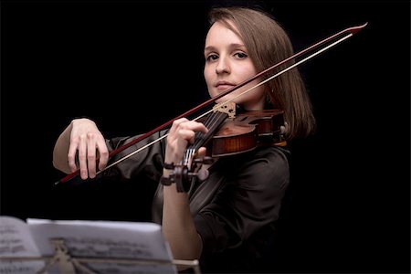 simsearch:400-09115438,k - Young beautiful woman violinist player playing her instrument on her shoulder holding bow. portrait in a blurred dark room in background. Concept of classical music Foto de stock - Super Valor sin royalties y Suscripción, Código: 400-09008940