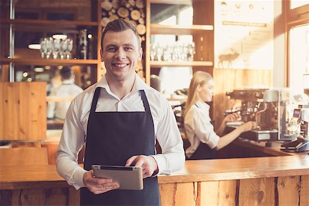 pouring cappuccino - Professional barista. Young woman in apron working at bar counter with coffee machine. Man using tablet computer Foto de stock - Super Valor sin royalties y Suscripción, Código: 400-09018950