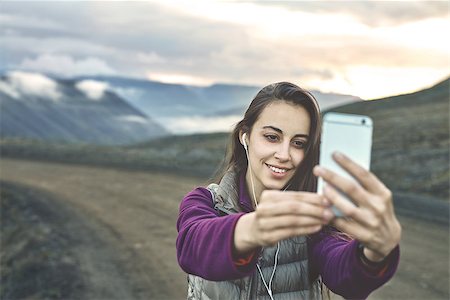 simsearch:400-08556910,k - Girl in warm clothing makes selfie photo on background of mountains and sea of Iceland. women on the road thru a mountain pass, fjord is on background Stock Photo - Budget Royalty-Free & Subscription, Code: 400-09011717