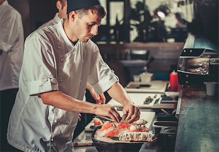 simsearch:400-08192842,k - One young white chef dressed in white uniform decorate ready dish in restaurant. He is working on maki rolls. Preparing traditional japanese sushi set in interior of modern professional kitchen Foto de stock - Super Valor sin royalties y Suscripción, Código: 400-09028840