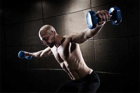 simsearch:400-08505882,k - Athletic muscular man training biceps with dumbbells on dark background Stock Photo - Budget Royalty-Free & Subscription, Code: 400-09029432