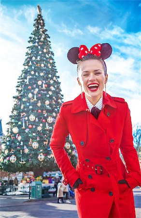 picture of a christmas tree in france - DISNEYLAND, FRANCE - DECEMBER, 8, 2016: Portrait of happy stylish woman in red trench coat standing in the front of big Christmas tree Photographie de stock - Aubaine LD & Abonnement, Code: 400-09029630