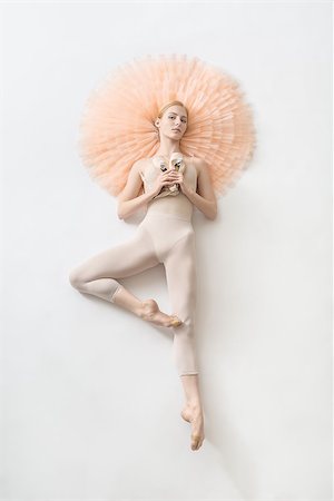simsearch:400-05739749,k - Young blonde ballerina lies in a passe on the peach tutu on the floor and holds pointe shoes in the studio. She wears a light dance wear and looks into the camera. Vertical. Photographie de stock - Aubaine LD & Abonnement, Code: 400-09029722