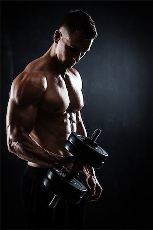 simsearch:400-05180877,k - Athletic shirtless young male fitness model makes exercises with dumbbells on dark background Stock Photo - Budget Royalty-Free & Subscription, Code: 400-09031297