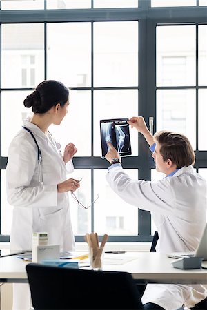 Experienced male orthopedist helping his female colleague with the interpretation of an X-ray of the knee of a patient in the office Fotografie stock - Microstock e Abbonamento, Codice: 400-09067693