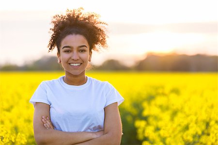 simsearch:400-04068097,k - Beautiful mixed race African American girl teenager female young woman happy smiling with perfect teeth at the end of a path in a field of yellow flowers Stockbilder - Microstock & Abonnement, Bildnummer: 400-09067838