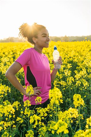 Outdoor portrait of beautiful happy mixed race African American girl teenager female young woman athlete runner drinking water from a bottle in a field of yellow flowers at sunset in golden evening sunshine Stock Photo - Budget Royalty-Free & Subscription, Code: 400-09069151